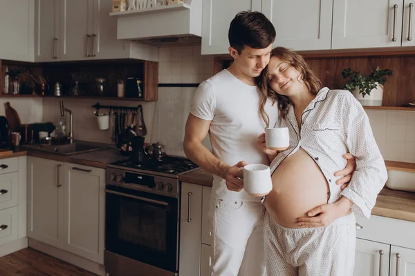 Boldog, fiatal terhes pár gazdaság bump hasa fehér pizsamában — Stock Fotó