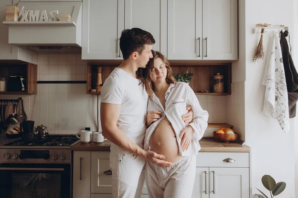 Happy νεαρό ζευγάρι έγκυος στο λευκό πιτζάμες κρατώντας την κοιλιά χτύπημα — Φωτογραφία Αρχείου