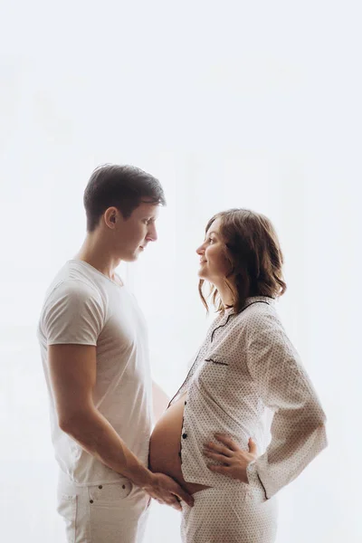 Feliz jovem grávida casal em pijama branco segurando barriga colisão — Fotografia de Stock