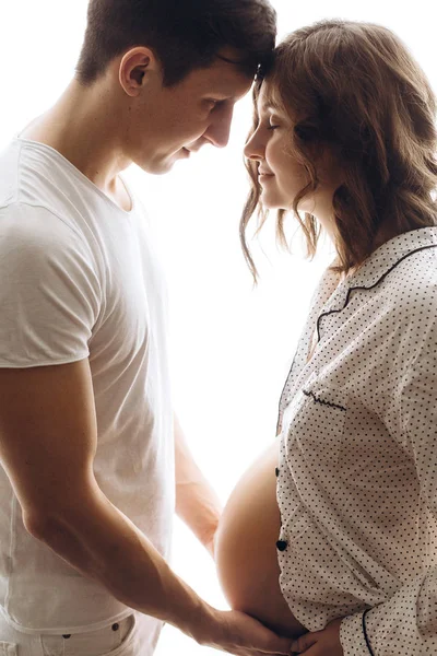 Feliz jovem grávida casal em pijama branco segurando barriga colisão — Fotografia de Stock