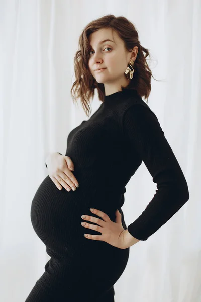 愉快的年轻孕妇在时尚的黑色礼服举行腹部 — 图库照片