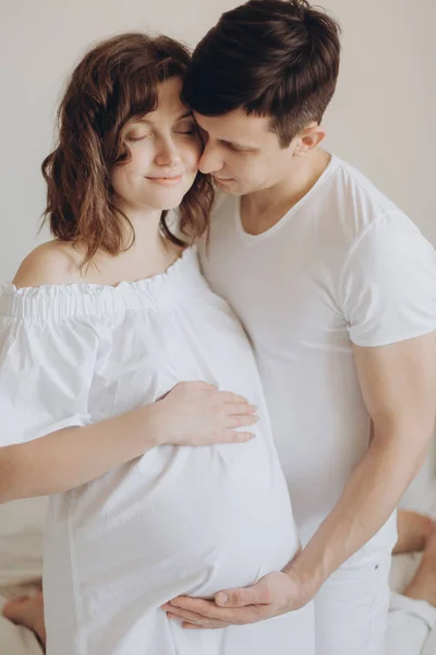 Щаслива вагітна пара розслабляється на білому ліжку і тримає живіт бу — стокове фото
