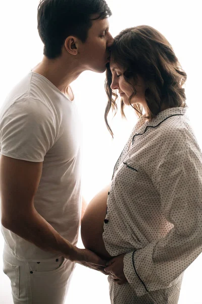 Щасливий молодий чоловік цілує свою вагітну дружину і тримає живіт — стокове фото