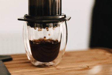 Aeropress ve cam fincan, ahşap masa, kahve kaşık clo düşer.
