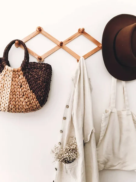 Stylish wooden hanger with straw bag, linen tote bag, brown hat — Stock Photo, Image