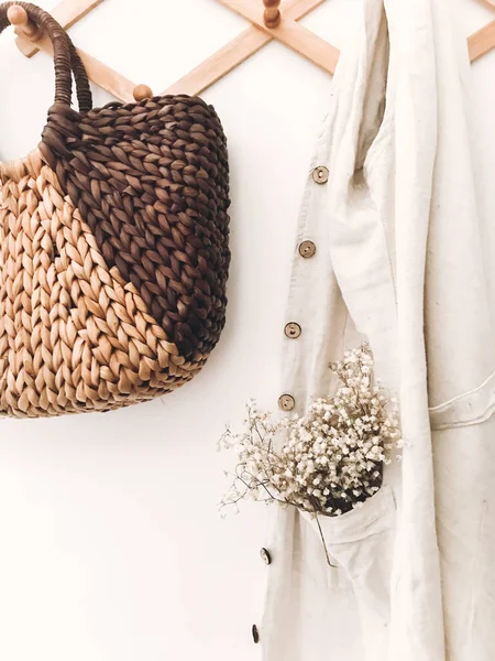 Elegante percha de madera con bolsa de paja, bolso de mano de lino, flores y — Foto de Stock