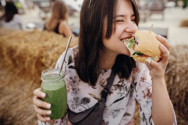 Fată elegantă hipster în ochelari de soare care mănâncă burger vegan delicios — Fotografie, imagine de stoc