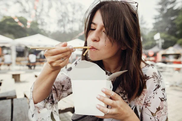 Elegante chica hipster comiendo fideos wok con verduras del coche — Foto de Stock