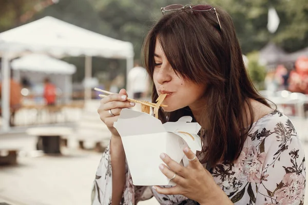 Stylish hipster girl eating wok noodles with vegetables from car — Stock Photo, Image