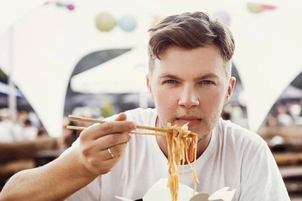 Stylish hipster man eating wok noodles with vegetables from cart