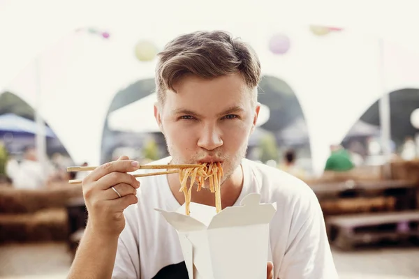 Stylish hipster man eating wok noodles with vegetables from cart