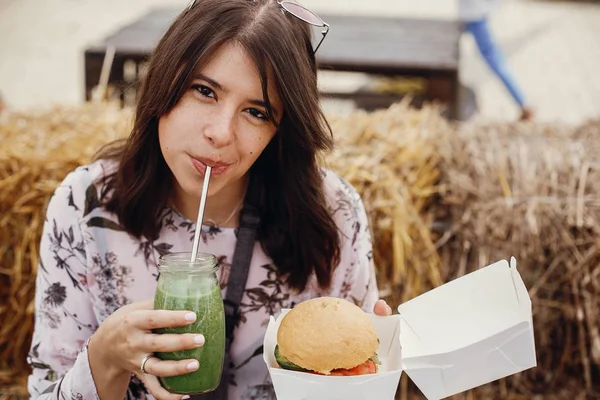 Стильная хипстерша с вкусным веганским бургером и выпивкой — стоковое фото