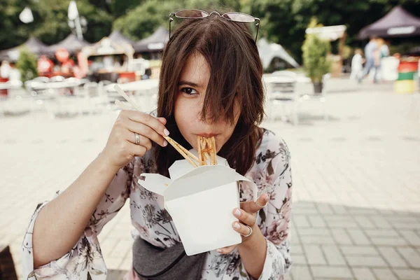 Stylish hipster girl eating wok noodles with vegetables from car — Stock Photo, Image