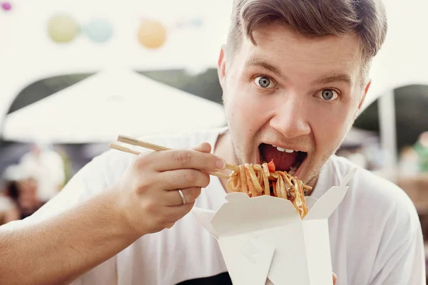 Стильный голодный мужчина ест вкусную вок-лапшу со смешными эмоти — стоковое фото