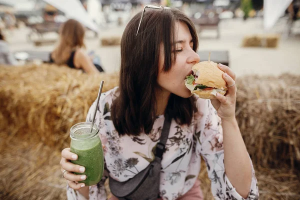 Fată elegantă hipster în ochelari de soare care mănâncă burger vegan delicios — Fotografie, imagine de stoc