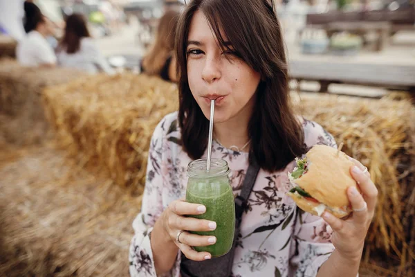 Elegante chica hipster sosteniendo deliciosa hamburguesa vegana y beber —  Fotos de Stock