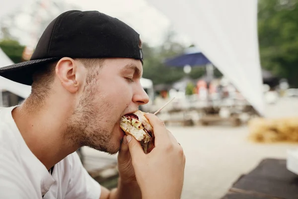 Elegante hombre hipster comiendo deliciosa hamburguesa vegana en la comida de la calle — Foto de Stock