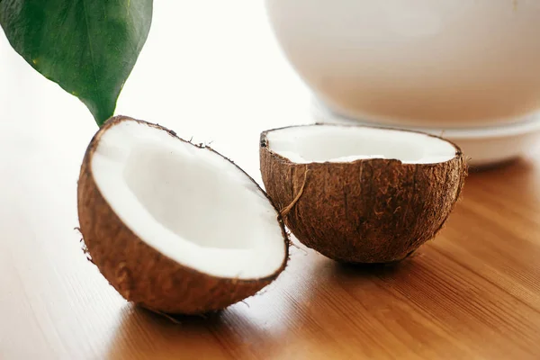 Halbierte Kokosnuss mit grünen Palmblättern auf Holztisch in weiß l — Stockfoto