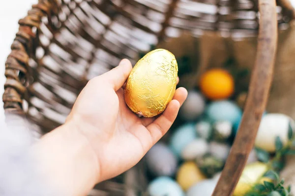 Рука держит золотое пасхальное яйцо и стильные яйца с зеленым баксом — стоковое фото