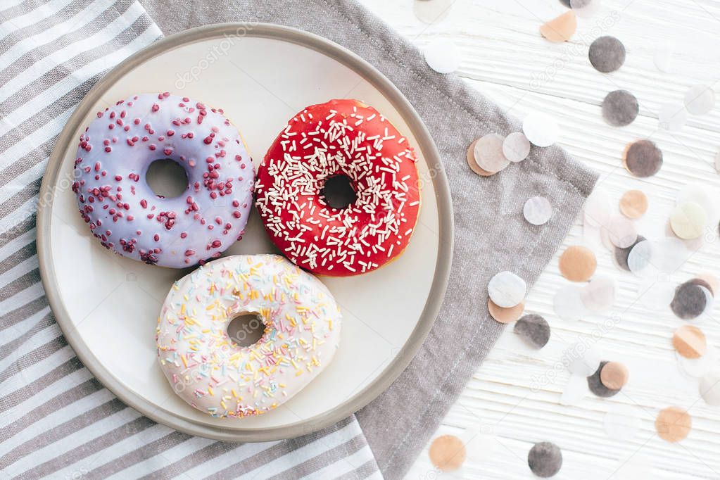 Delicious colorful donuts with sprinkles on stylish plate on whi
