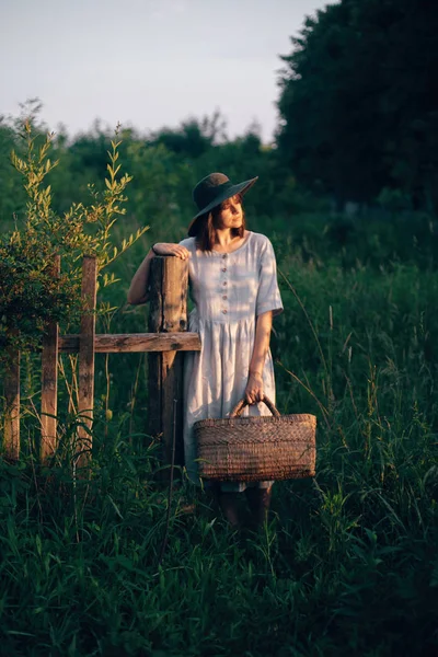 Menina elegante em vestido de linho segurando cesta de palha rústica no woode — Fotografia de Stock