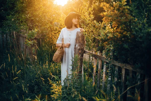 Menina elegante em vestido de linho segurando cesta de palha rústica no woode — Fotografia de Stock