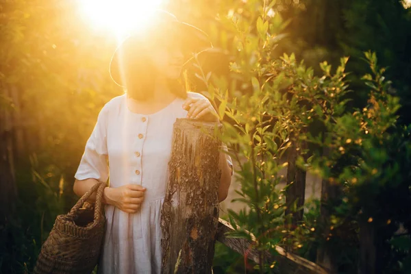 Stylish girl in linen dress holding rustic straw basket at woode — Stock Photo, Image