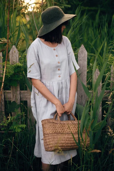 Stylish girl in linen dress holding rustic straw basket at woode — Stock Photo, Image