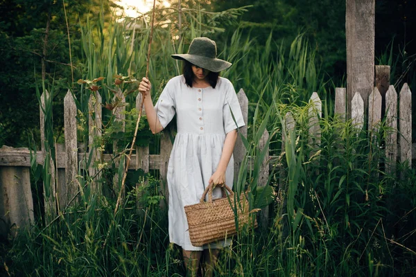 Стильна дівчина в лляній сукні тримає сільський солом'яний кошик біля вугрів — стокове фото