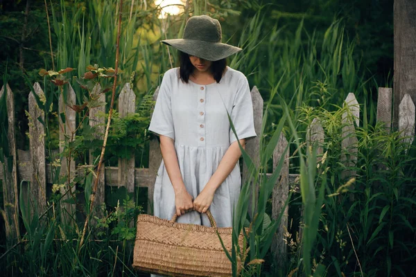 Stylish girl in linen dress holding rustic straw basket at woode — Stock Photo, Image