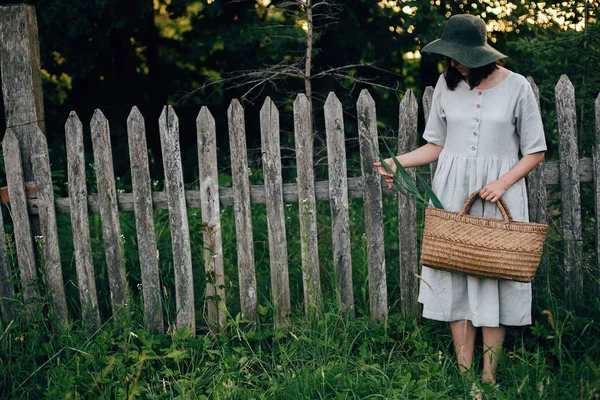 Stylish girl in linen dress holding rustic straw basket with gre — Stock Photo, Image