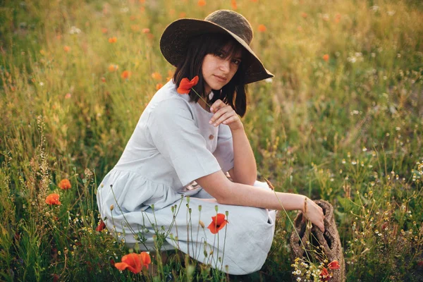 Stylish girl in linen dress holding poppy flower in meadow in su — Stock Photo, Image