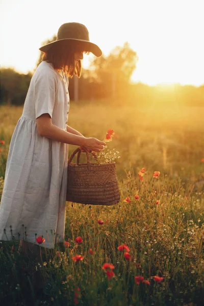 Stylish girl in linen dress gathering flowers in rustic straw ba — Stock Photo, Image