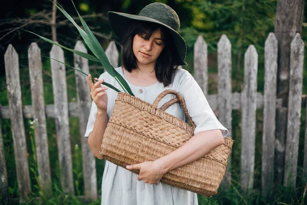 Stylish girl in linen dress holding rustic straw basket with gre Stock Picture