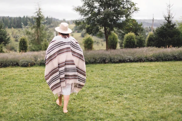 Elegante chica hipster en poncho, vestido de lino y sombrero caminando en l —  Fotos de Stock