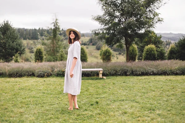 Stijlvolle hipster meisje in linnen jurk en hoed lopen op lavendel — Stockfoto