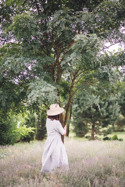 Stylish hipster girl in linen dress and hat relaxing in lavender — Stock Photo, Image