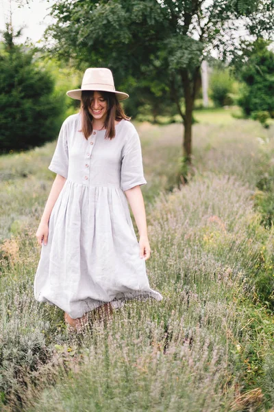 Stylish hipster girl in linen dress and hat walking in lavender — Stock Photo, Image