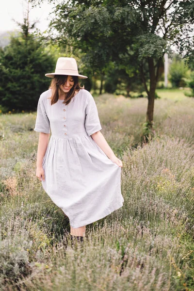 Stylish hipster girl in linen dress and hat walking in lavender — Stock Photo, Image