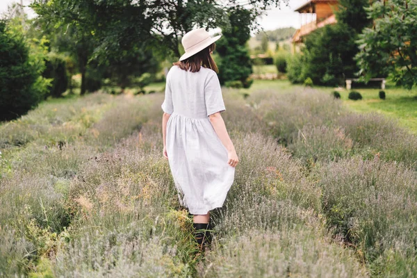 Gadis hipster bergaya dengan gaun linen dan topi berjalan di lavender — Stok Foto