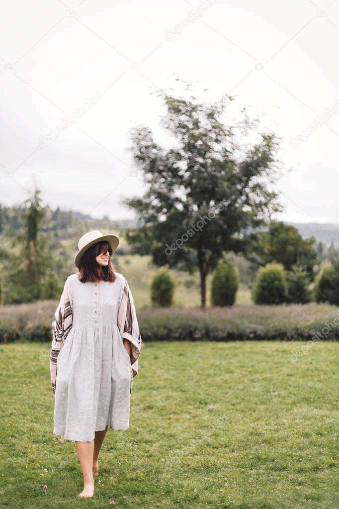 Stylish hipster girl in linen dress and hat walking at lavender 