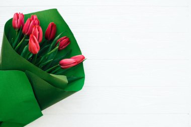 Beyaz ahşap sırt üzerinde yeşil kağıt güzel kırmızı lale buketi
