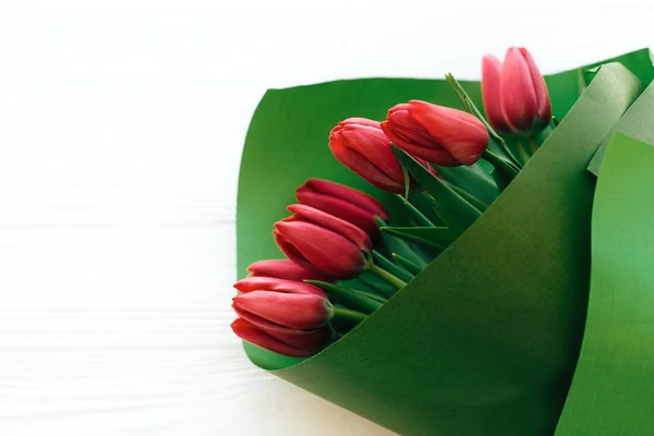 Bonito buquê de tulipas elegantes em papel verde em madeira branca — Fotografia de Stock