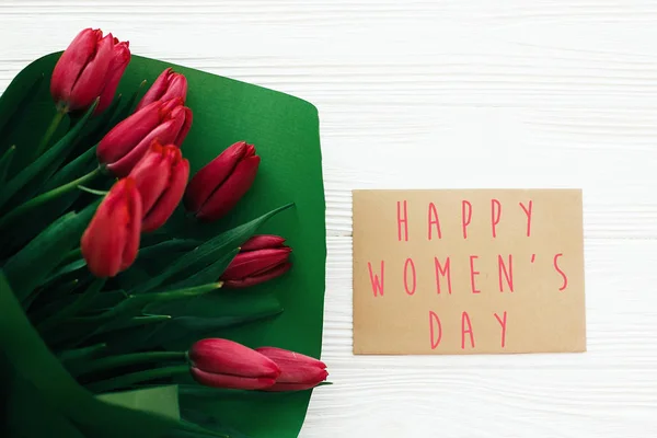 Happy Women 's Day text și lalele roșii frumoase pe lemn alb — Fotografie, imagine de stoc