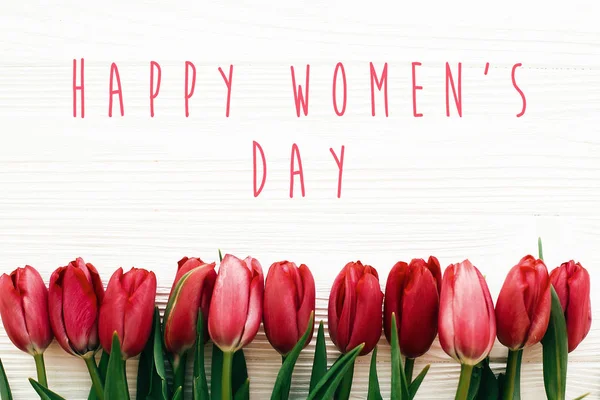 Texto del Día de la Mujer Feliz y hermosos tulipanes rojos sobre madera blanca — Foto de Stock