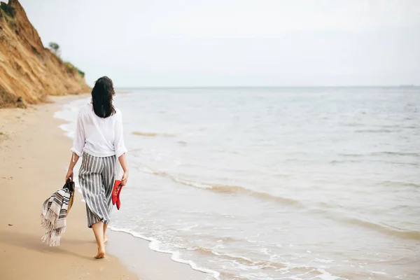 Elegante hipster menina andando descalça na praia, segurando saco e — Fotografia de Stock