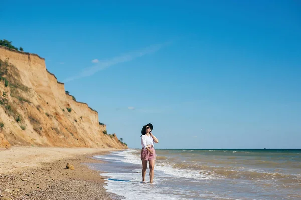 Stylisches Hipster-Mädchen mit Hut, das am Strand spazieren geht und lächelt. Sommer — Stockfoto