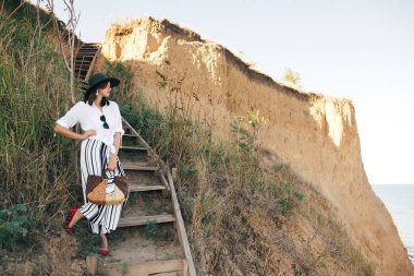 Şık boho kız şapka s yakın çim ile kumlu uçurumda poz