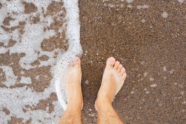 Ayaklar kum üzerinde köpük dalgalar köpük ayakta, üst görünümü. Sıcak adam ayak