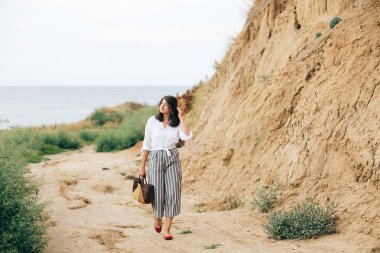 Tropik adada yürüyen beyaz gömlekli mutlu genç boho kadın